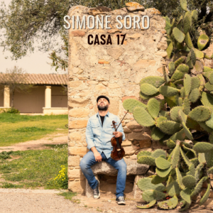 Simone Soro sitting against an old stone wall with his violin, surrounded by nature.